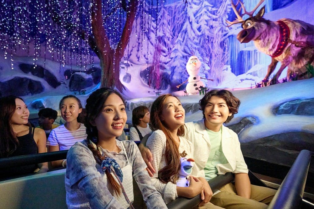 한 무리의 사람들이 반짝이는 조명과 눈사람 캐릭터로 겨울을 테마로 한 어트랙션을 즐깁니다.