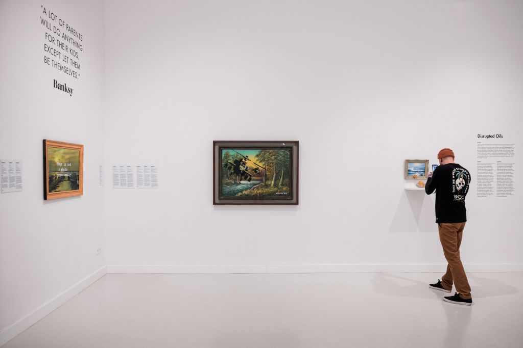 흰색 벽에 두 개의 그림이 있는 미니멀한 갤러리 공간입니다. 사람은 오른쪽에서 부분적으로 볼 수 있습니다.