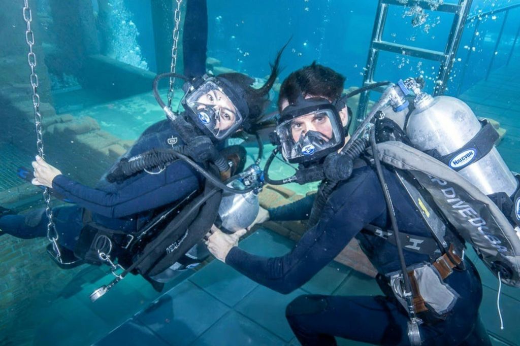 수영장에서 풀 기어를 갖춘 두 명의 스쿠버 다이버가 사다리를 배경으로 장비를 잡고 있습니다.