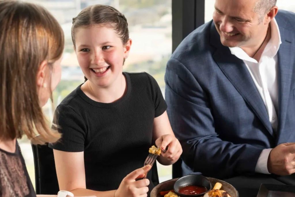 어린 소녀와 어른이 미소를 지으며 함께 식탁에 앉아 음식을 먹습니다. 여기에는 디핑 소스 한 그릇도 포함됩니다.