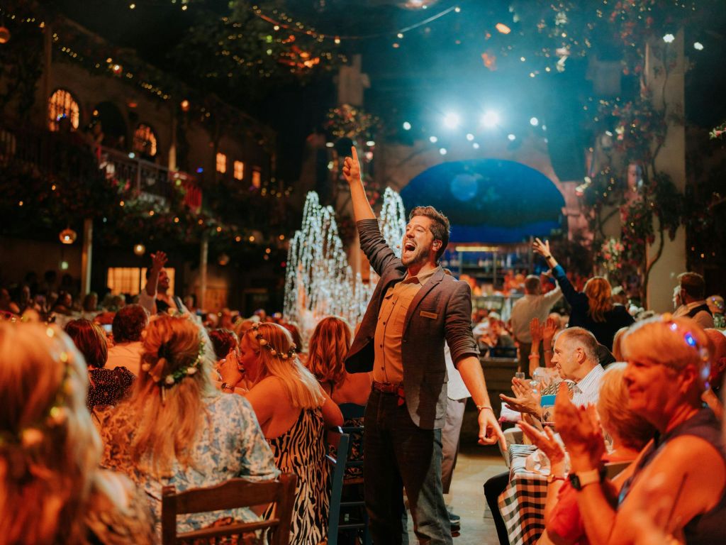 사람들이 축제와 조명이 잘 켜진 장소에서 식사하고 축하하는 활기찬 장면으로 공연자가 군중을 사로잡습니다.