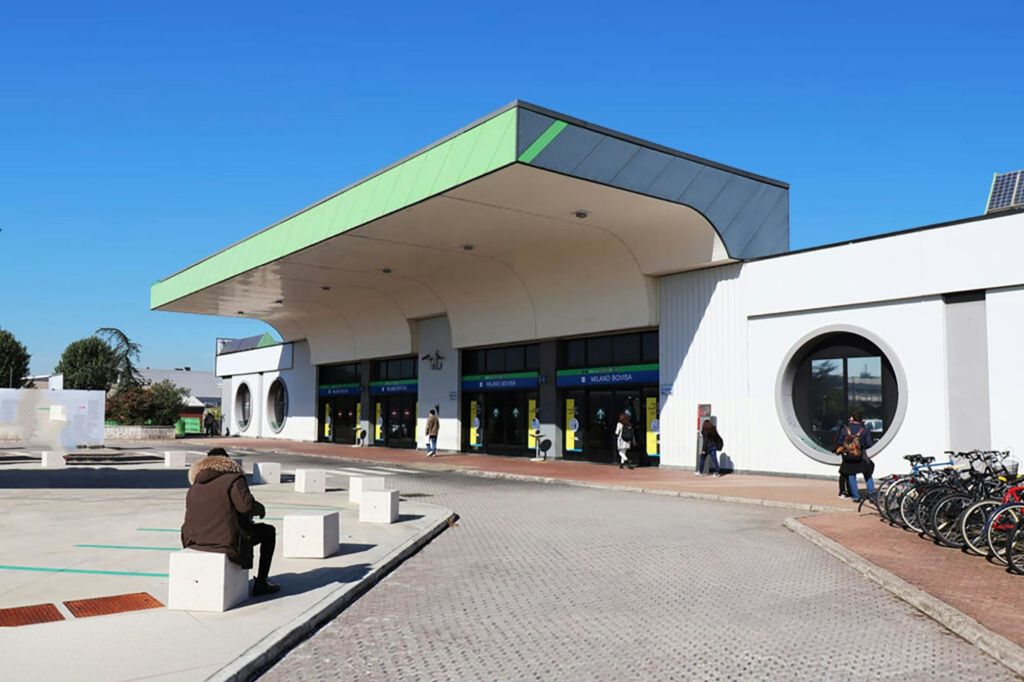 초록색 지붕의 출입구, 원형 창문, 맑고 푸른 하늘 아래 앞을 걷는 사람들이 있는 현대적인 건물입니다.