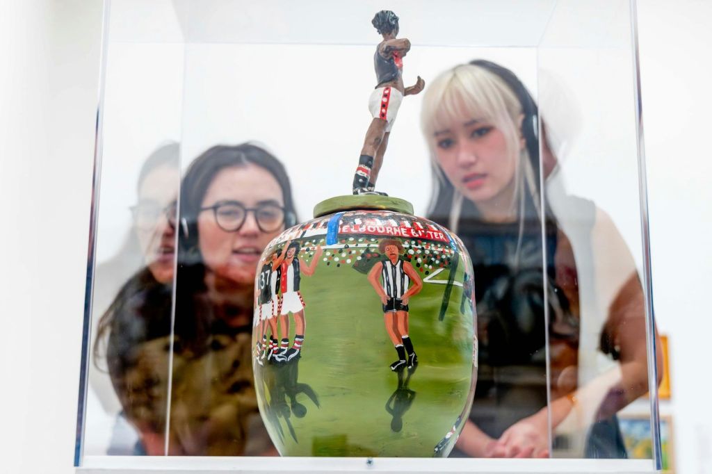 두 사람이 유리 케이스에 표시된 스포츠 장면을 묘사한 장식된 세라믹 꽃병을 관찰합니다.