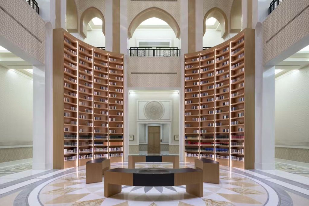 높이 굽은 책장, 중앙 테이블, 화려한 천장 디자인이 돋보이는 현대적인 도서관 인테리어입니다.