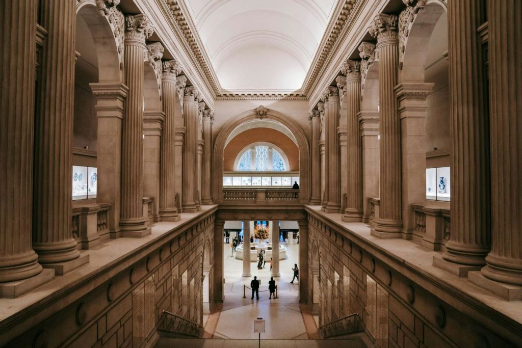 높은 기둥, 아치형 통로, 디테일한 천장이 있는 그랜드 홀. 사람들은 아래층과 위층의 거리에서 볼 수 있습니다.