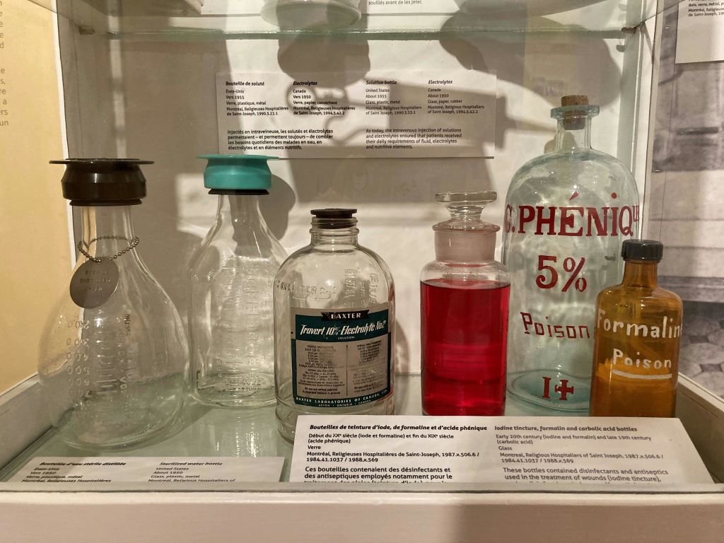 투명 액체와 적색 액체가 들어 있는 다양한 빈티지 병이 진열된 진열 선반으로, 과학 및 의학 텍스트로 표시되어 있습니다.