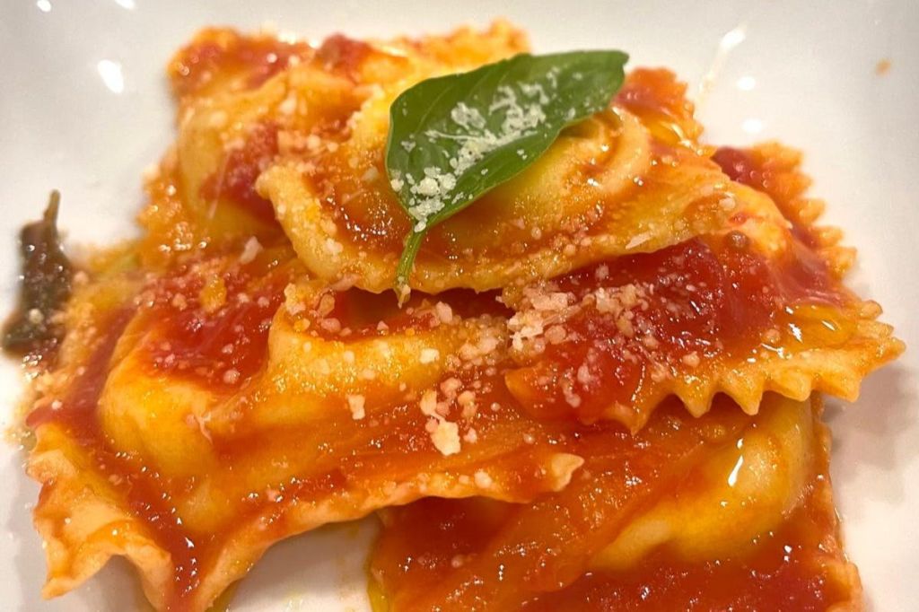 토마토 소스, 강판에 간 파르메산, 그 위에 신선한 바질 잎을 곁들인 치즈 라비올리의 클로즈업.