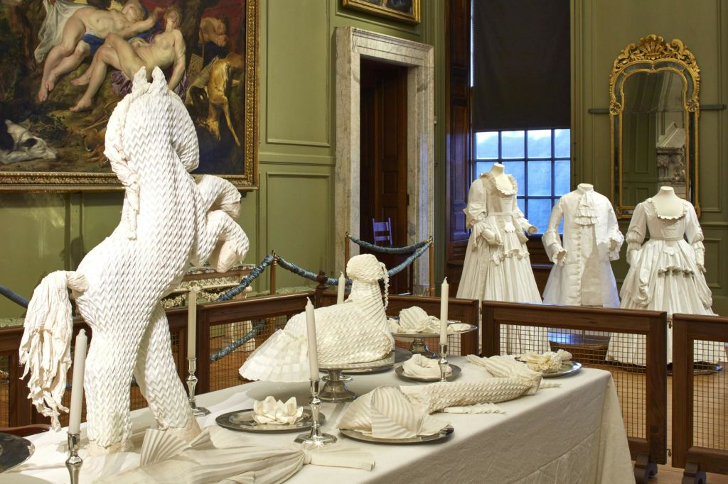 마네킹을 배경으로 정교하게 접힌 흰색 냅킨과 가운이 놓인 화려한 객실입니다.