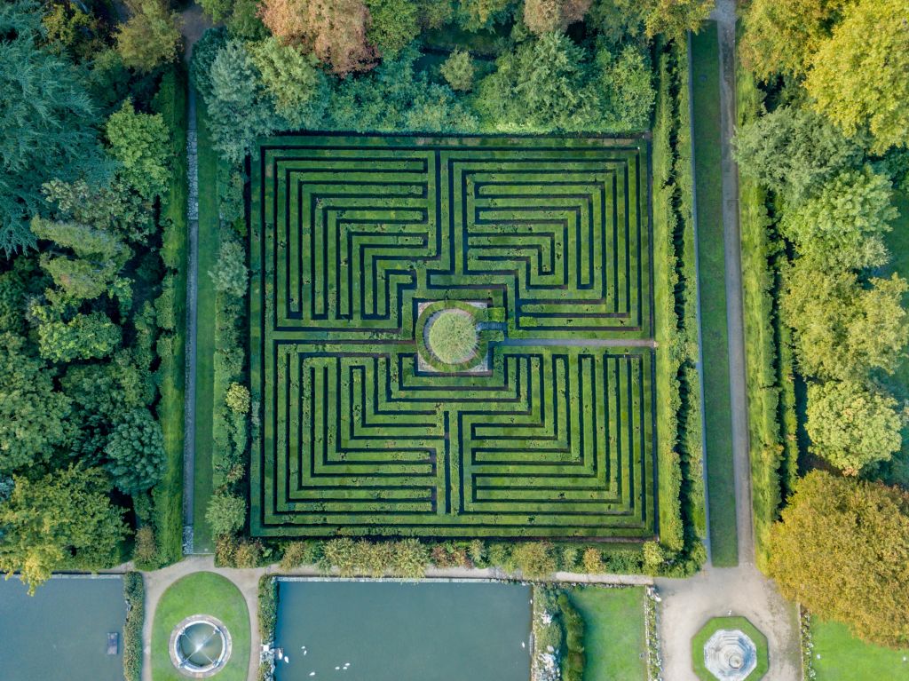 나무, 통로, 인근 연못으로 둘러싸인 정원의 크고 대칭적인 울타리 미로의 공중 전망.