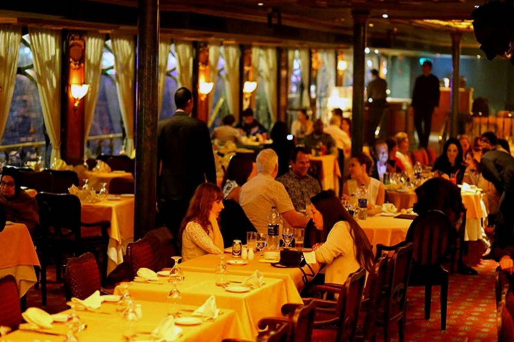 테이블에 앉아 대화를 나누고 음식과 음료를 제공하는 종업원이 있는 따뜻하고 붐비는 레스토랑입니다.