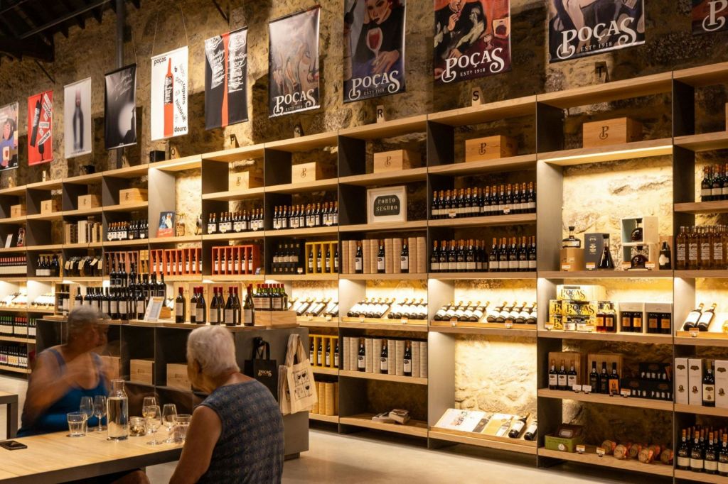 병과 와인 박스가 진열된 나무 선반이 있는 와인 숍 인테리어. 한 사람이 전경의 테이블에 앉아 있습니다.