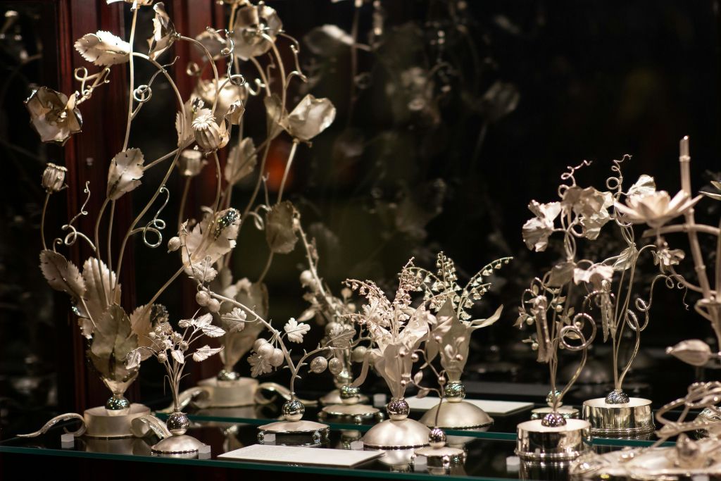 어둡고 흐릿한 배경이 있는 반사 표면에 정교하게 세공된 금속 꽃 조각.