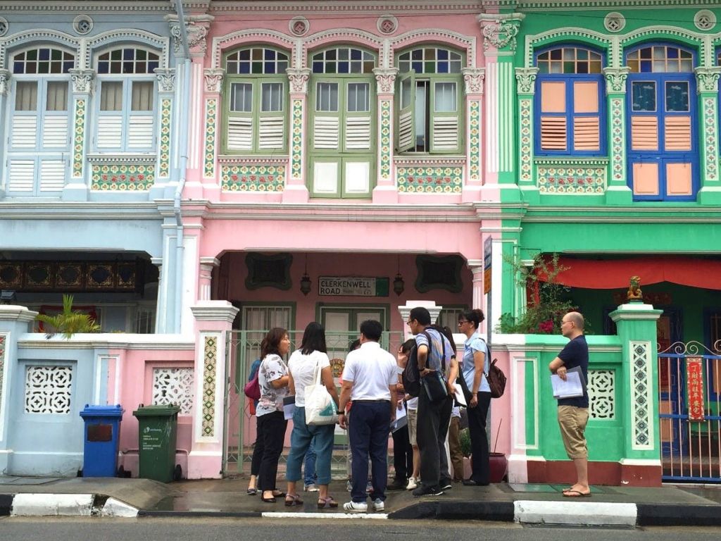 분홍색과 초록색 외관, 장식용 창문이 있는 화려하고 화려하게 꾸며진 건물 앞에 한 무리의 사람들이 서 있습니다.