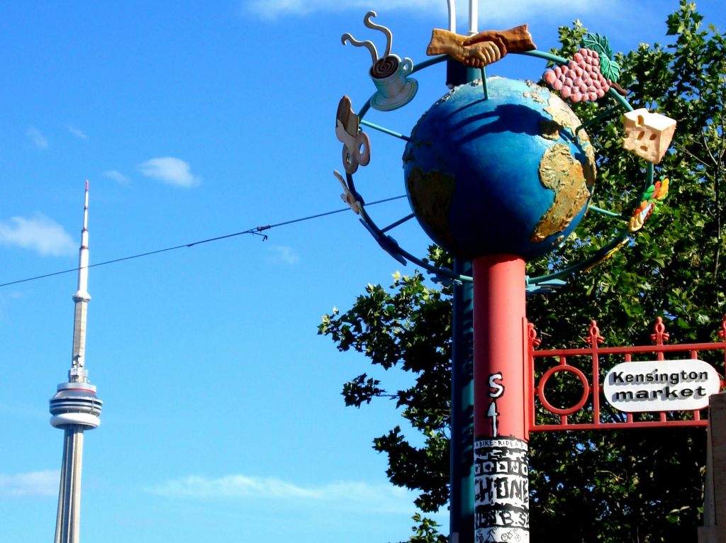 푸른 하늘과 나무를 배경으로 지구본과 커피잔, 프레첼 등 다양한 조형물이 있는 표지판.