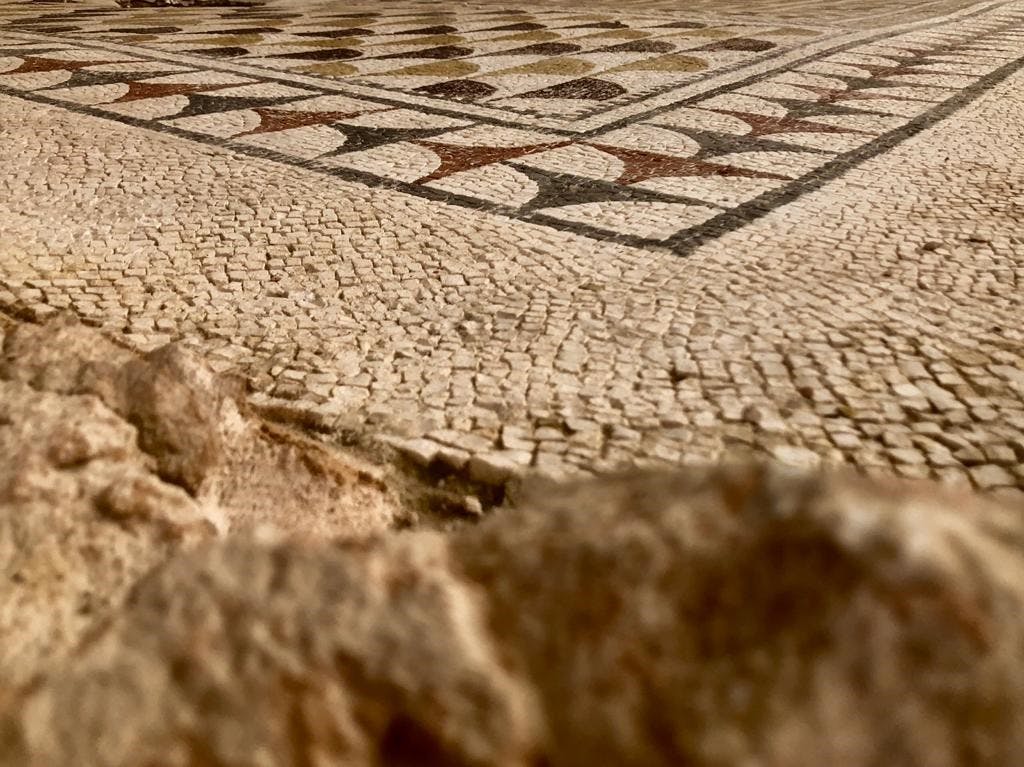 크림색, 갈색 및 회색 타일의 조합이 특징인 복잡한 기하학적 패턴이 있는 고대 모자이크 타일 바닥의 클로즈업.