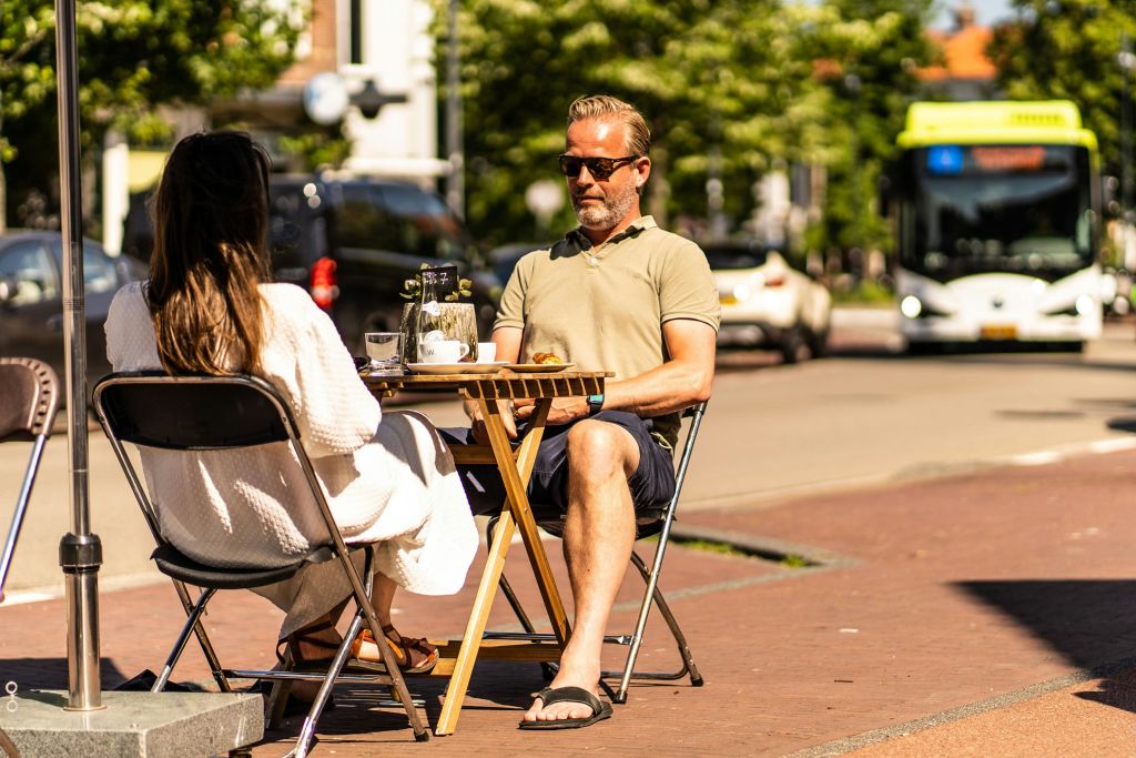 햇빛과 거리 풍경을 배경으로 야외 카페 테이블에 앉아 있는 두 사람.