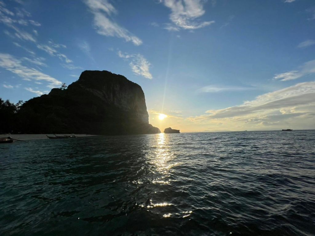 왼쪽은 어두운 절벽, 태양을 반사하는 잔잔한 물, 부분적으로 흐린 하늘이 있는 바다 위로 석양을 감상할 수 있습니다.