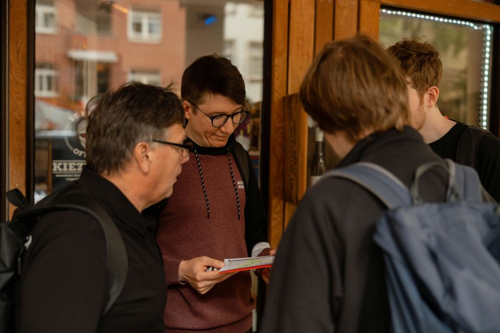 세 사람이 상점 밖에 서 있습니다. 한 남자는 팜플렛을 읽고 다른 남자는 팜플렛을 봅니다.
