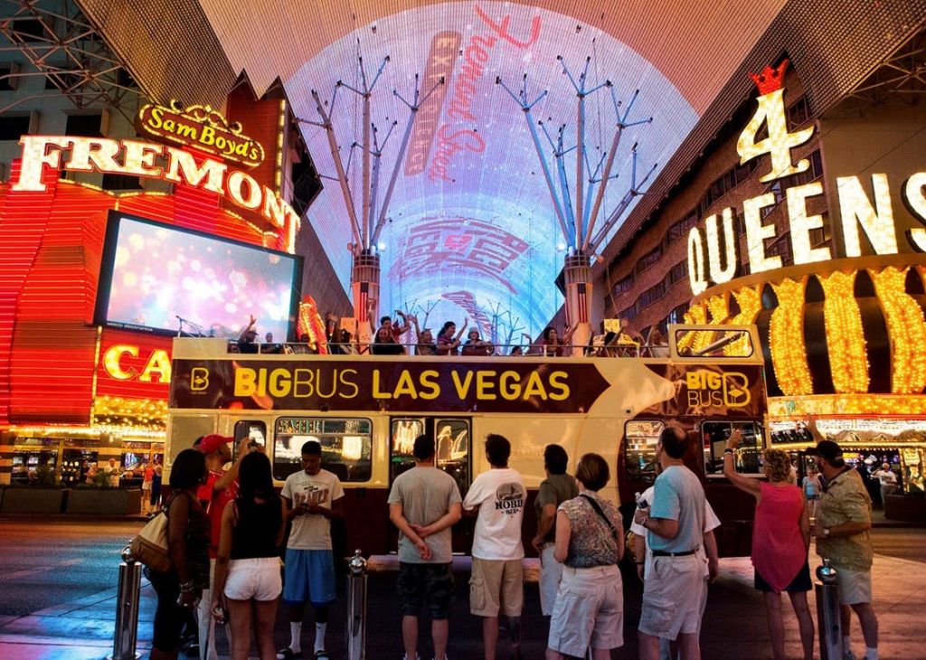 밤에는 라스베이거스의 프리몬트 스트리트 익스피리언스 (Fremont Street Experience) 의 조명 표지판 아래 빅 버스 라스베이거스 투어 버스 옆에 군중이 모여듭니다.