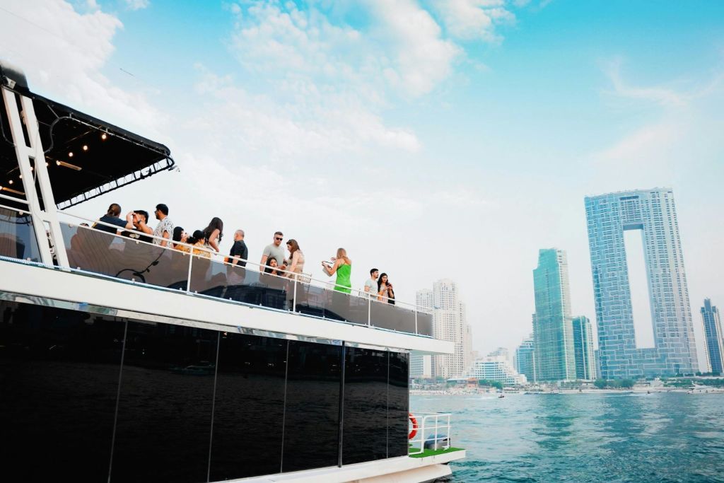 도시의 고층 건물과 푸른 하늘을 배경으로 보트 상단 갑판에서 어울리는 사람들.