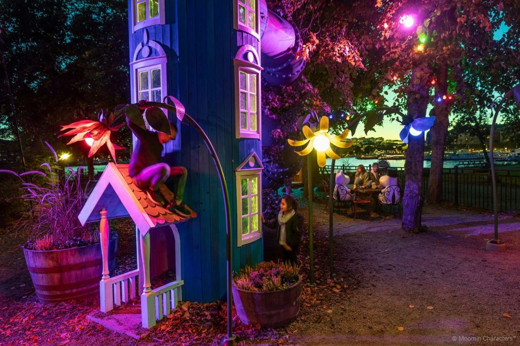 형형색색의 조명, 푸른 극장, 나무 조각상, 테이블을 배경으로 사람들의 시선을 사로잡는 기발한 야외 풍경.