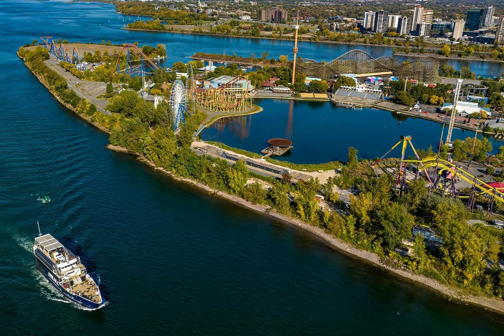 녹음과 도시 경관으로 둘러싸인 물가 근처에 놀이기구와 관광지가 있는 놀이공원의 공중 전망.