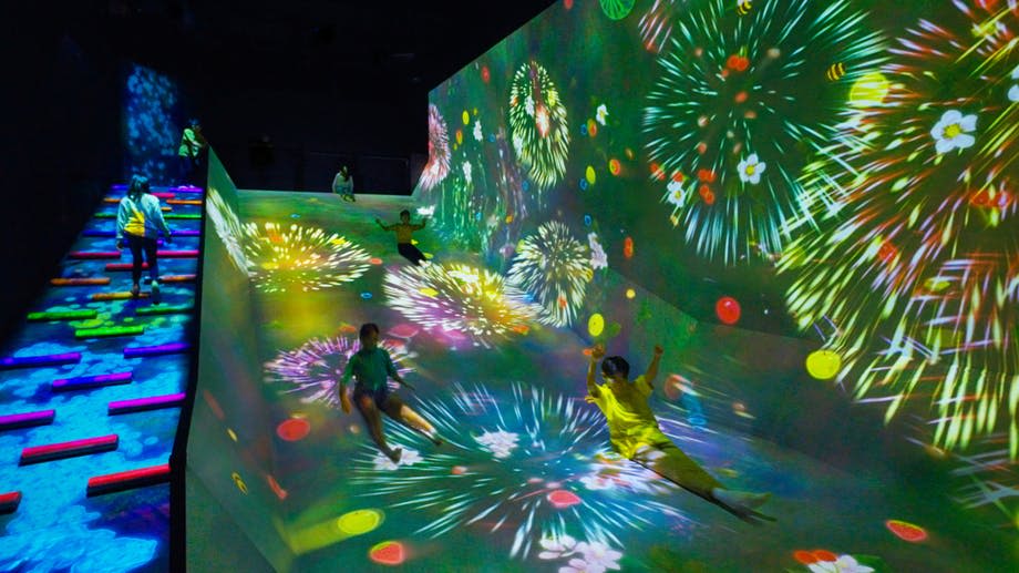 어두운 방에서 다채로운 불꽃놀이와 꽃이 투영된 조명이 켜진 경사면을 따라 미끄러져 내려오는 아이들.