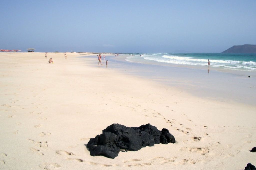 사람들은 부드러운 파도가 치는 모래 해변을 따라 흩어져 있었고, 앞에는 검은 바위 더미가 있었습니다.