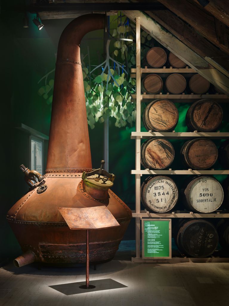 구리 증류 주전자는 배경에 단풍이 보이는 지하실의 오래된 나무 통 선반 옆에 있습니다.