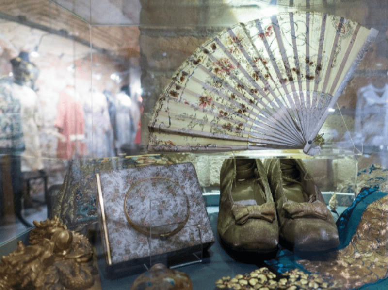 장식용 선풍기, 활이 달린 빈티지 신발, 꽃무늬 핸드백 및 기타 골동품 액세서리가 들어 있는 디스플레이 케이스.