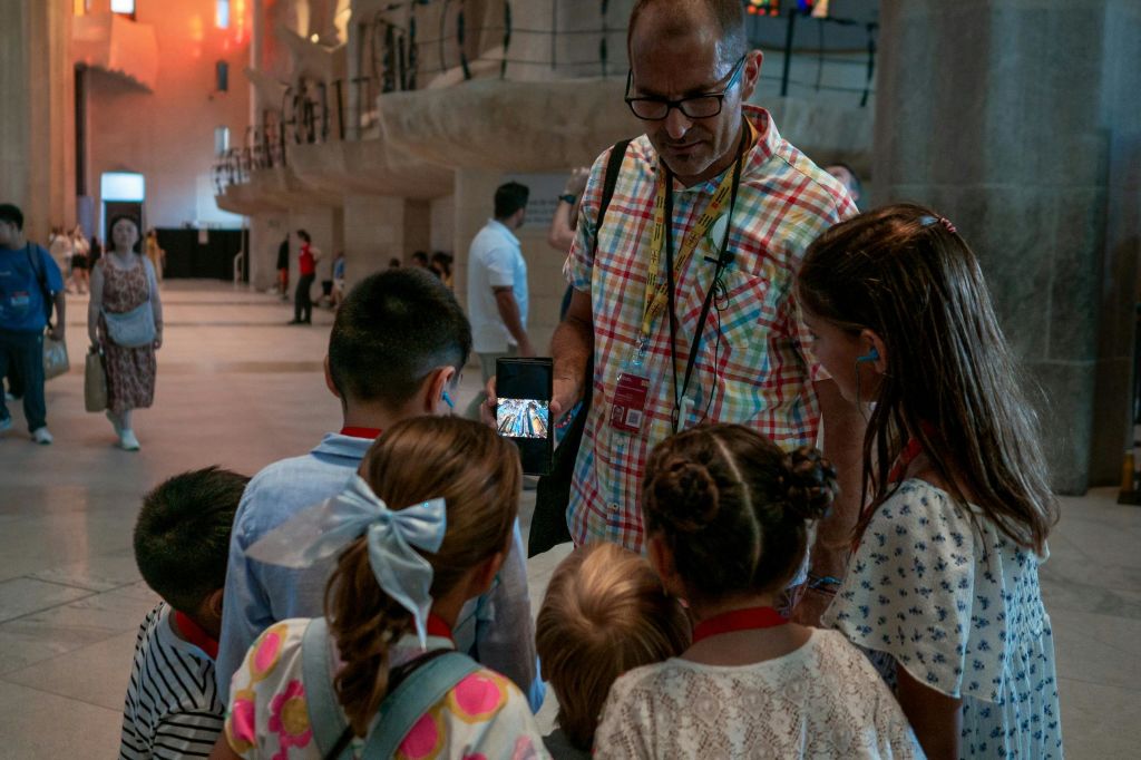 높은 천장과 화려한 조명이 있는 현대적인 대형 건물 내부에서 한 남성이 어린이들에게 휴대폰을 보여줍니다.