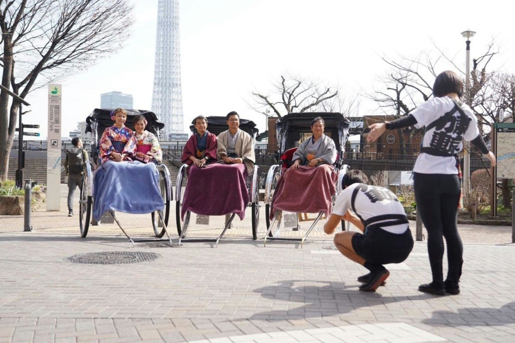전통 복장을 한 네 명이 인력거에 앉아 담요를 뒤집어 쓴 채 웅크린 자세로 사진을 찍고 있습니다.