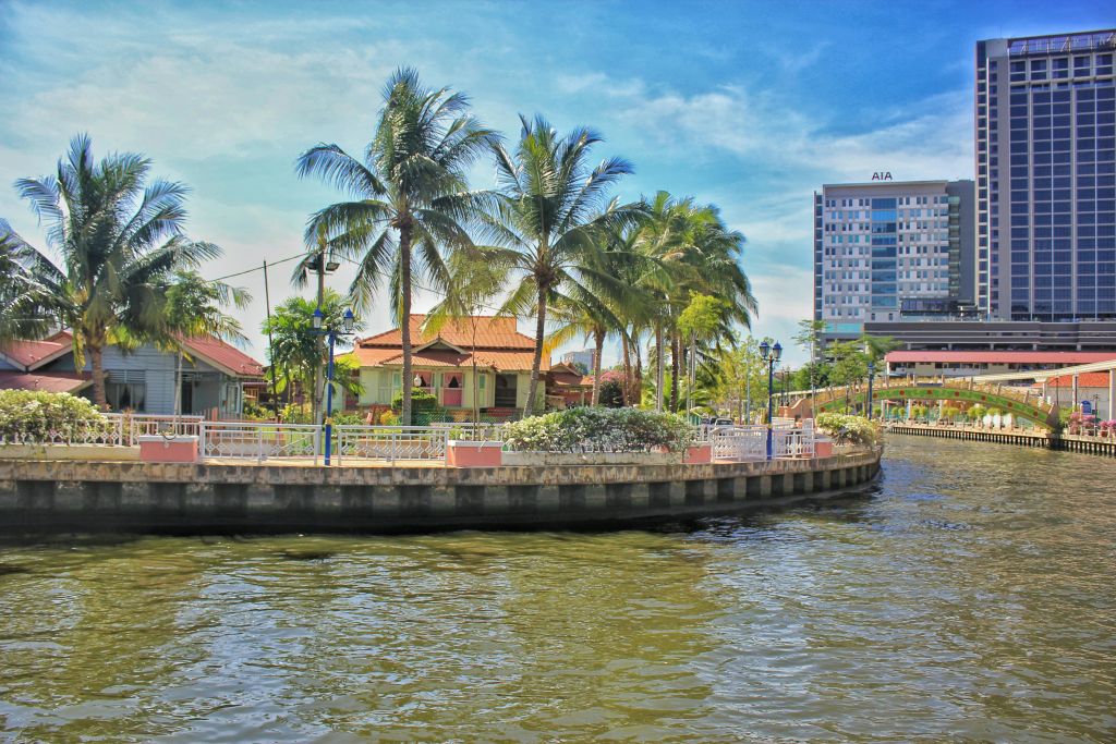 야자수, 붉은 지붕의 건물, 맑고 푸른 하늘을 배경으로 한 현대적인 고층 건물이 있는 강변 풍경.