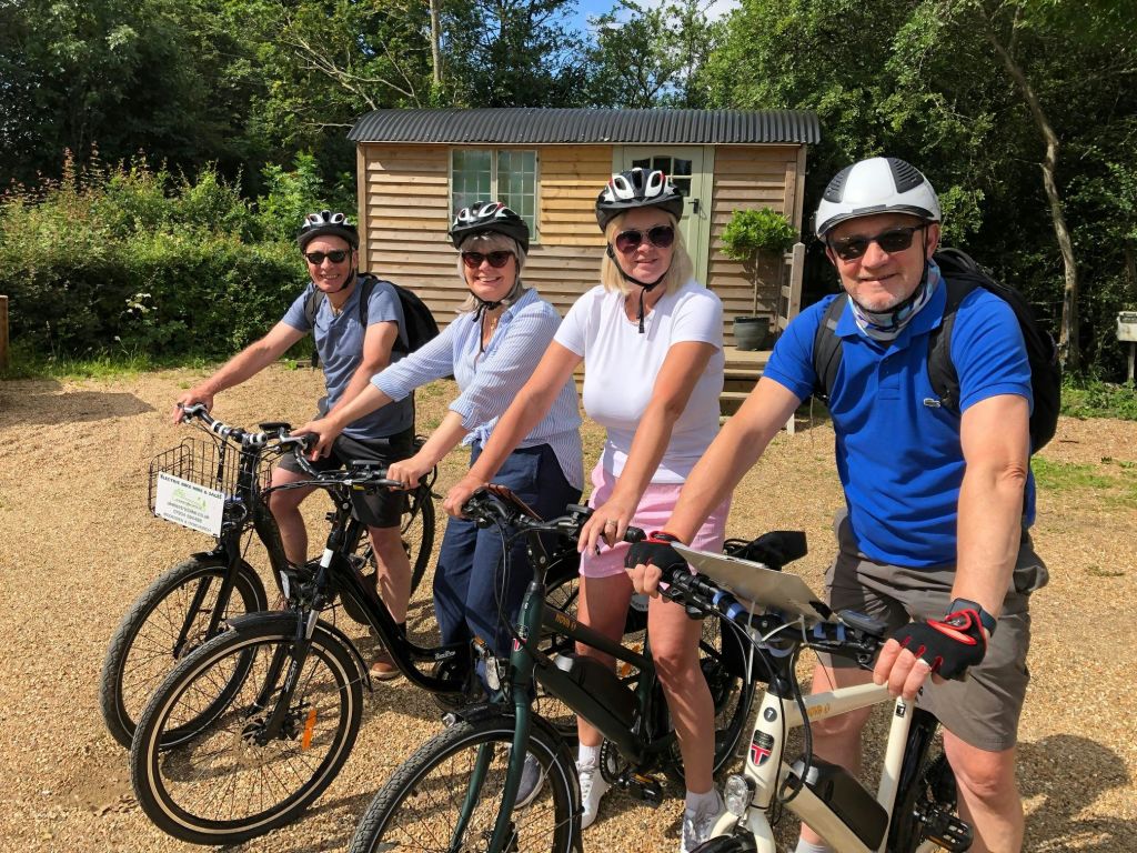 자전거를 탄 네 명이 나무로 둘러싸인 나무 오두막 앞에 서서 자전거를 타고 있습니다.