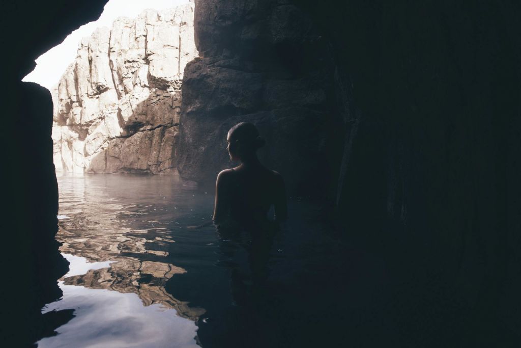 한 사람이 바위 벽이 있는 희미한 불빛이 비치는 동굴 안의 물 속에서 허리를 감싸고 서 있습니다. 위쪽 개구부에서 빛이 흘러 들어옵니다.