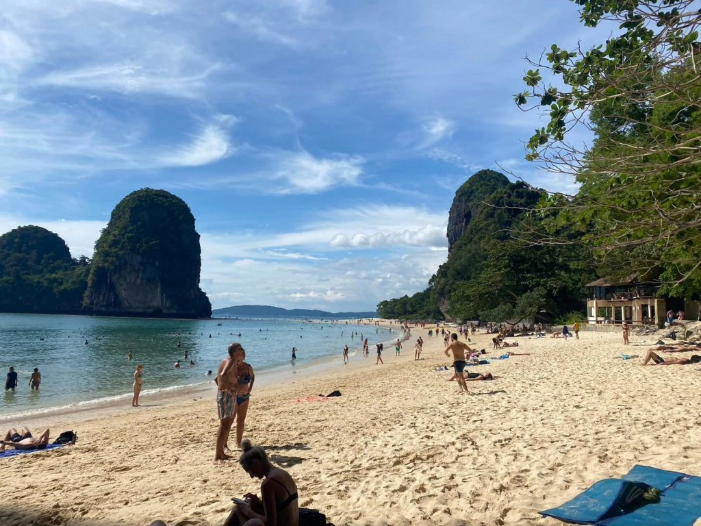 두 개의 커다란 암석을 배경으로 모래 해변에서 화창한 하루를 보내고, 수영하고, 일광욕을 즐기고, 휴식을 취하는 사람들.