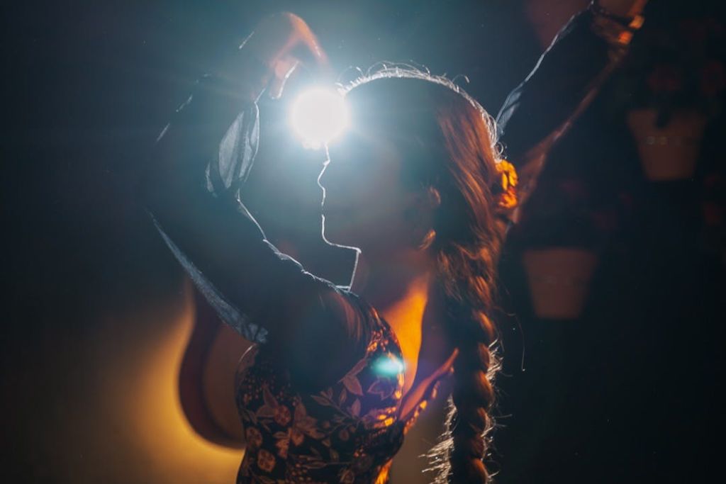 땋은 헤어스타일을 한 사람이 손을 통해 빛나는 밝은 빛에 비추어 팔을 들어 올려 극적인 실루엣을 연출합니다.