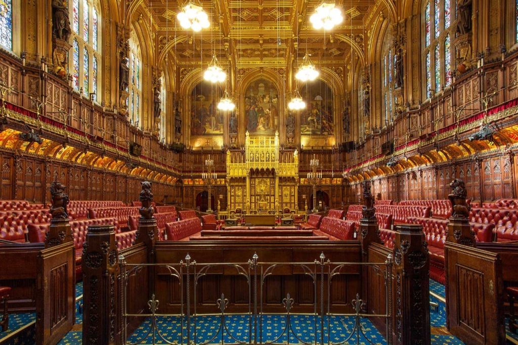 높은 천장과 샹들리에, 빨간색 덮개로 덮인 벤치, 복잡한 목공예품, 커다란 스테인드글라스 창문이 있는 화려한 방.