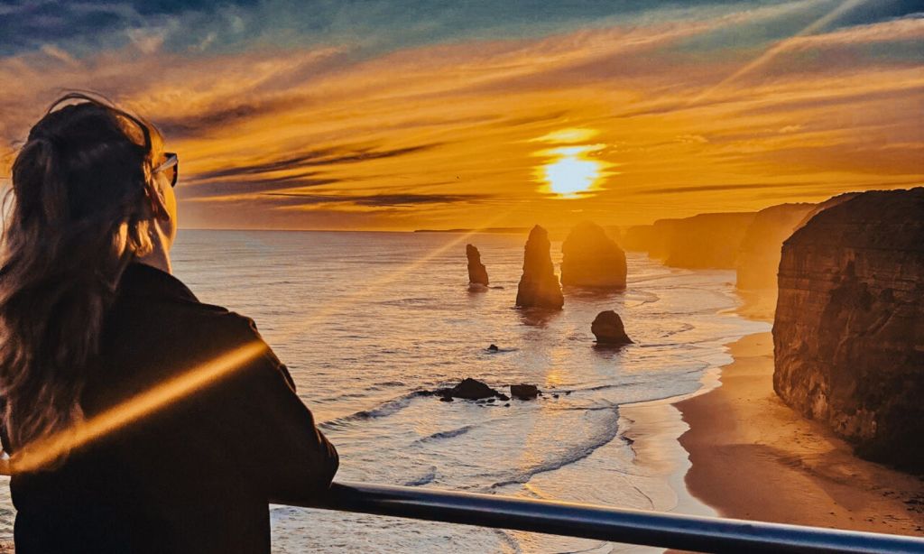 바다에서 황금빛 오렌지빛 석양을 감상하며 바다 더미가 내려다보이는 난간에 기대어 있는 사람.