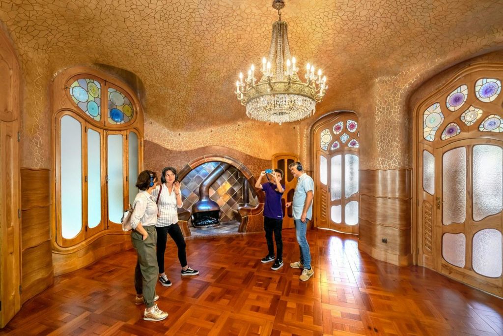 4명이 대형 샹들리에, 스테인드글라스 창문, 장식 벽난로가 있는 아르누보식 방을 둘러봅니다.