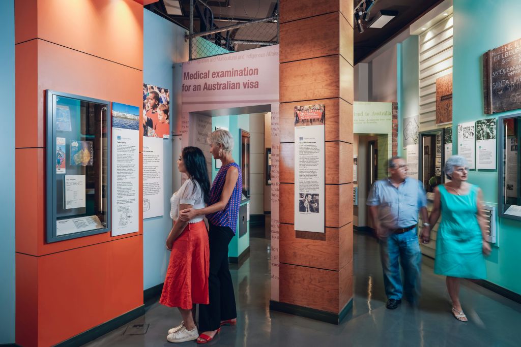 벽에 간판, 사진, 정보 패널이 전시된 호주 이민 관련 전시회를 둘러보고 있습니다.