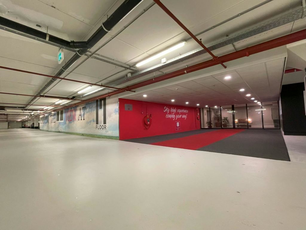 천장에 파이프와 조명이 노출된 실내의 넓은 빈 공간, 왼쪽 벽에 벽화, 오른쪽에 레드 카펫이 있습니다.