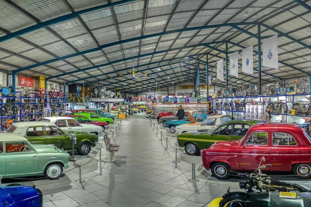 넓은 실내 빈티지 자동차 박물관에는 천장이 높은 대형 금속 지붕 아래 다채로운 클래식 자동차가 줄지어 있습니다.