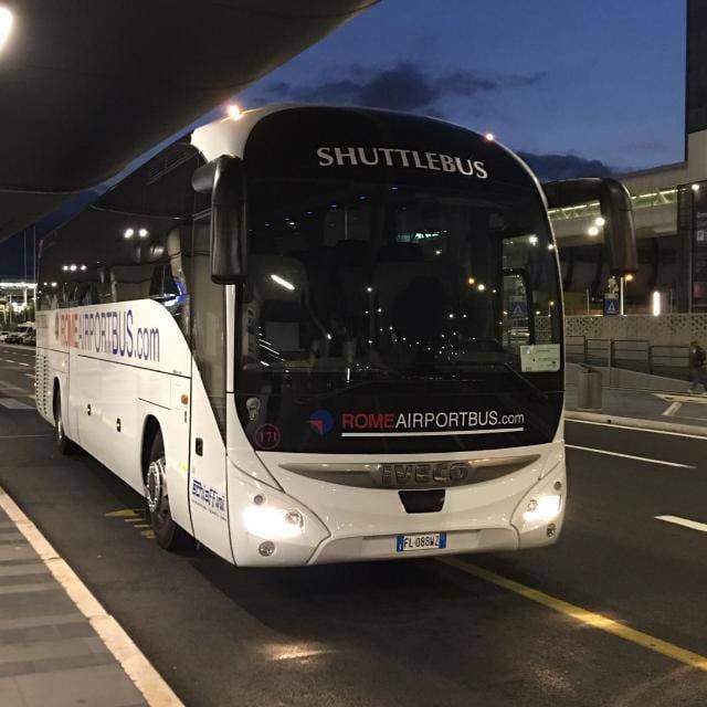 외부에 "ROME AIRPORTBUS.com" 과 "SHUTTLEBUS" 가 있는 터미널 승차장에 셔틀 버스가 주차되어 있습니다.