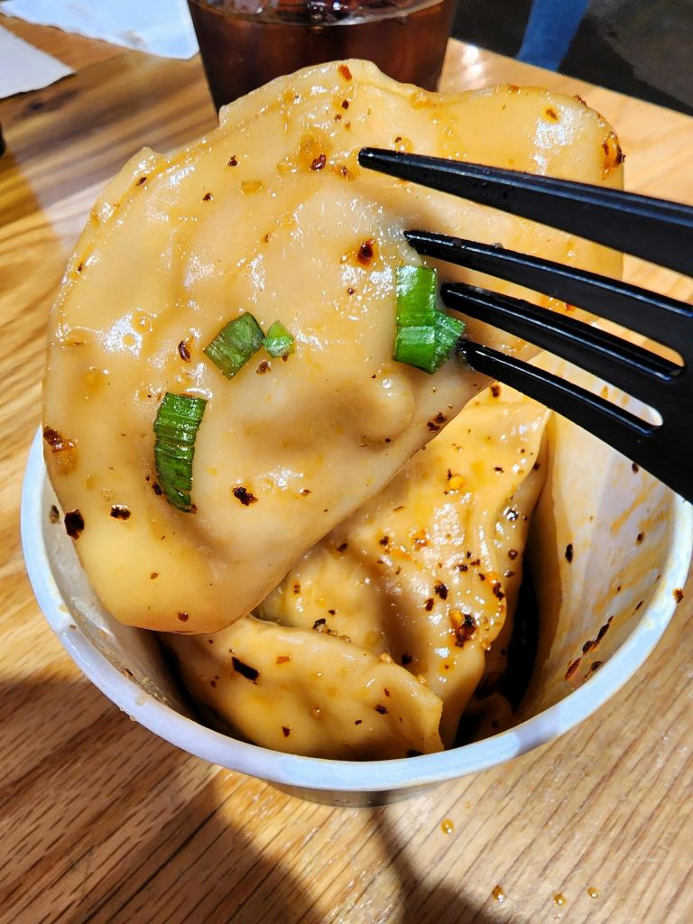 소스에 담긴 만두를 클로즈업한 것으로, 대파로 장식하고 검은 포크가 나무 테이블 위에 놓은 컵 위에 올려놓습니다.