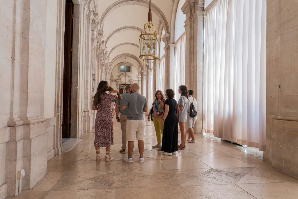 아치형 천장과 높고 깎아지른 듯한 커튼이 있는 넓고 조명이 밝은 복도에서 사람들이 서서 이야기를 나누고 있습니다.