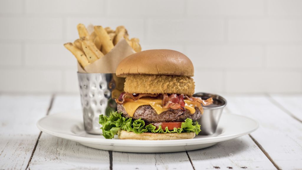 베이컨, 치즈, 양상추, 튀긴 양파 링을 곁들인 햄버거를 금속 컵과 디핑 소스에 곁들인 접시에 담았습니다.