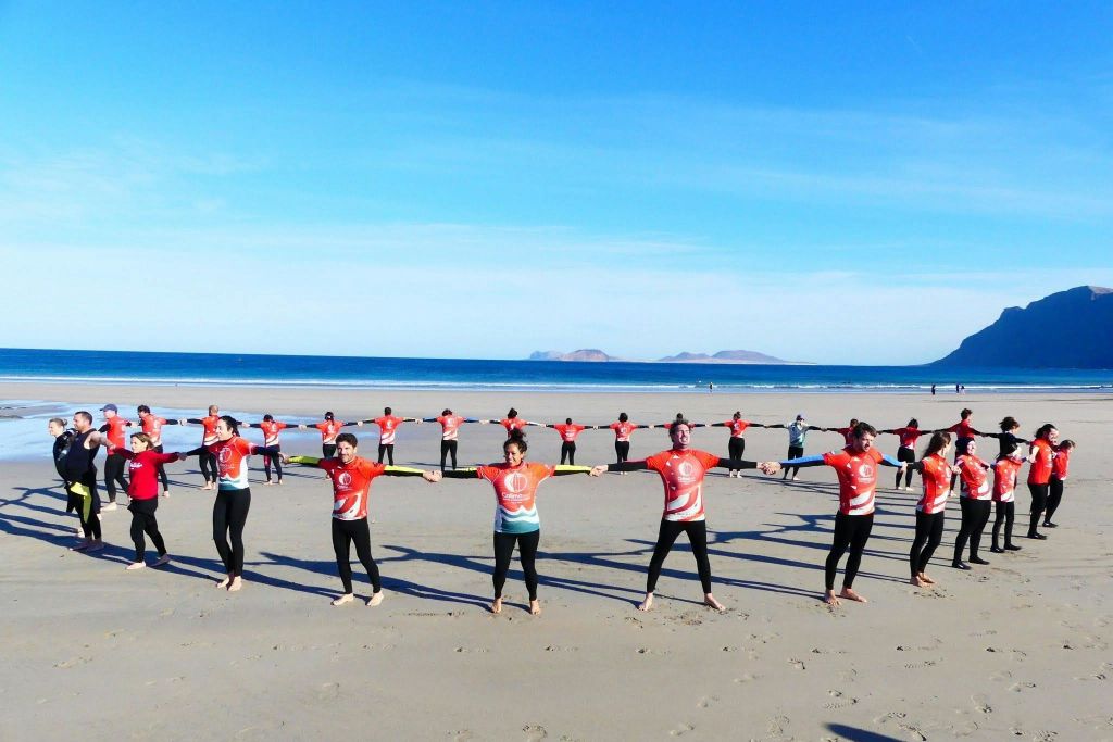 해변에서 빨간색 셔츠와 검은색 바지를 입고 맑고 푸른 하늘 아래 일렬로 손을 잡고 있는 한 무리의 사람들.