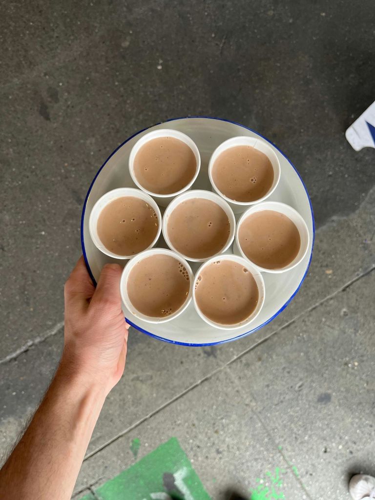 회색 콘크리트 표면에 놓인 음료와 같은 갈색 액체 6컵이 담긴 트레이를 들고 있는 손.