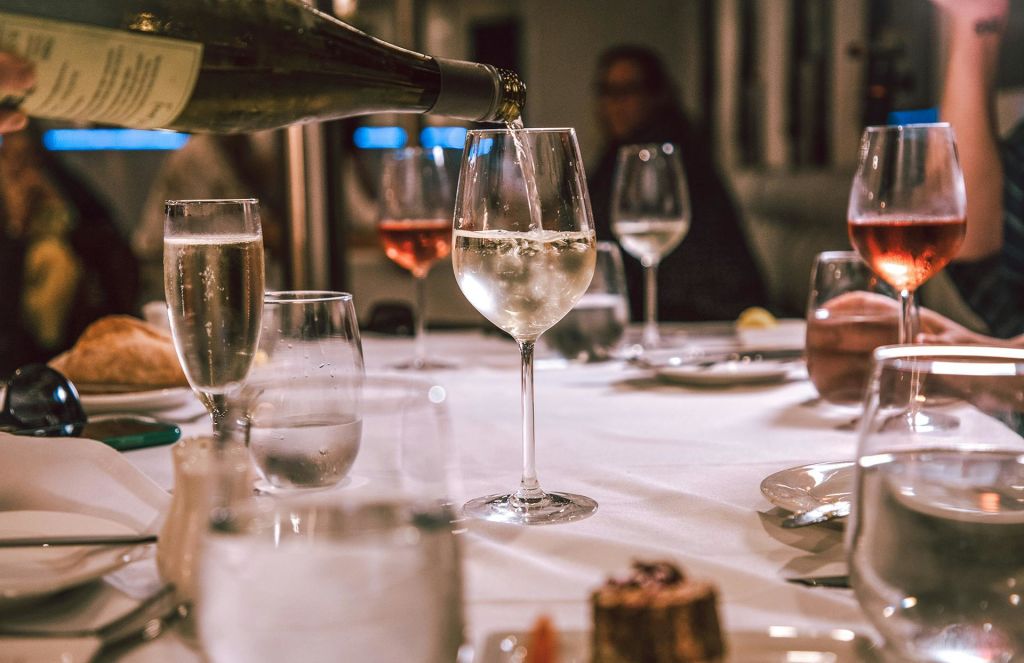 유리잔과 접시, 전경의 디저트가 놓인 식탁 위에 놓인 유리잔에 와인을 붓고 있습니다.